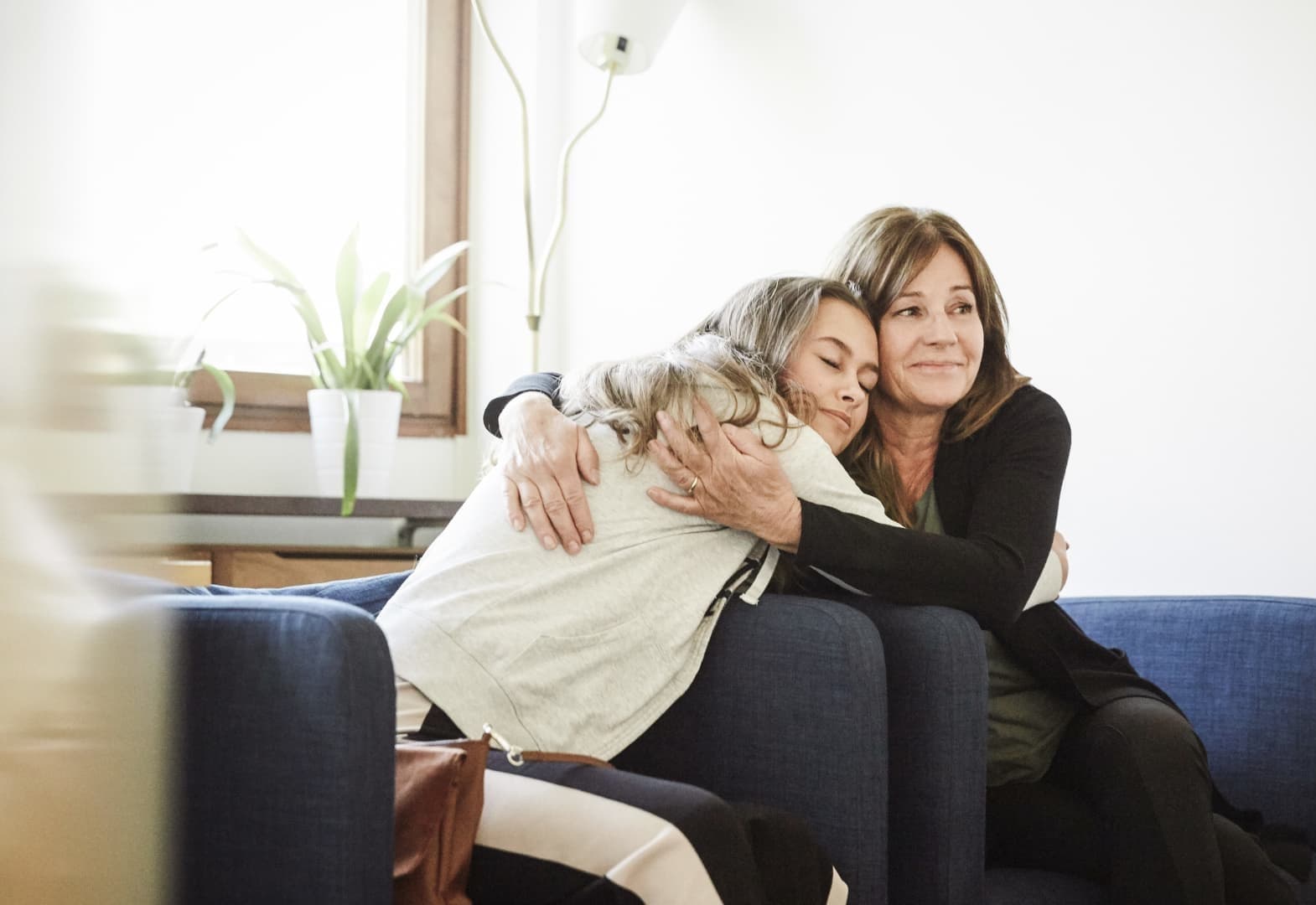 A woman and a young girl sharing a warm, emotional embrace on a blue sofa.