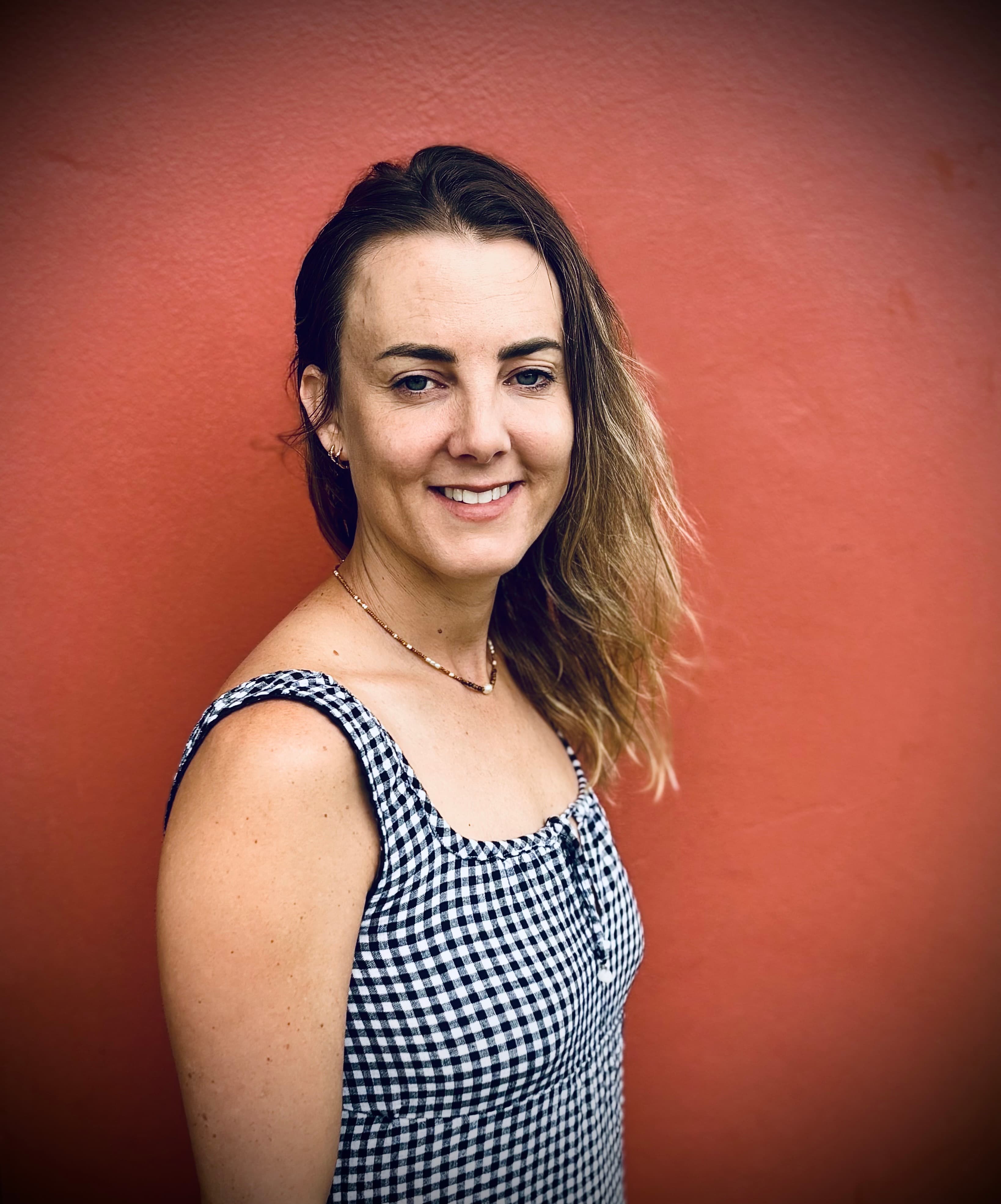 Smiling woman wearing a black and white checkered dress against a solid red wall.