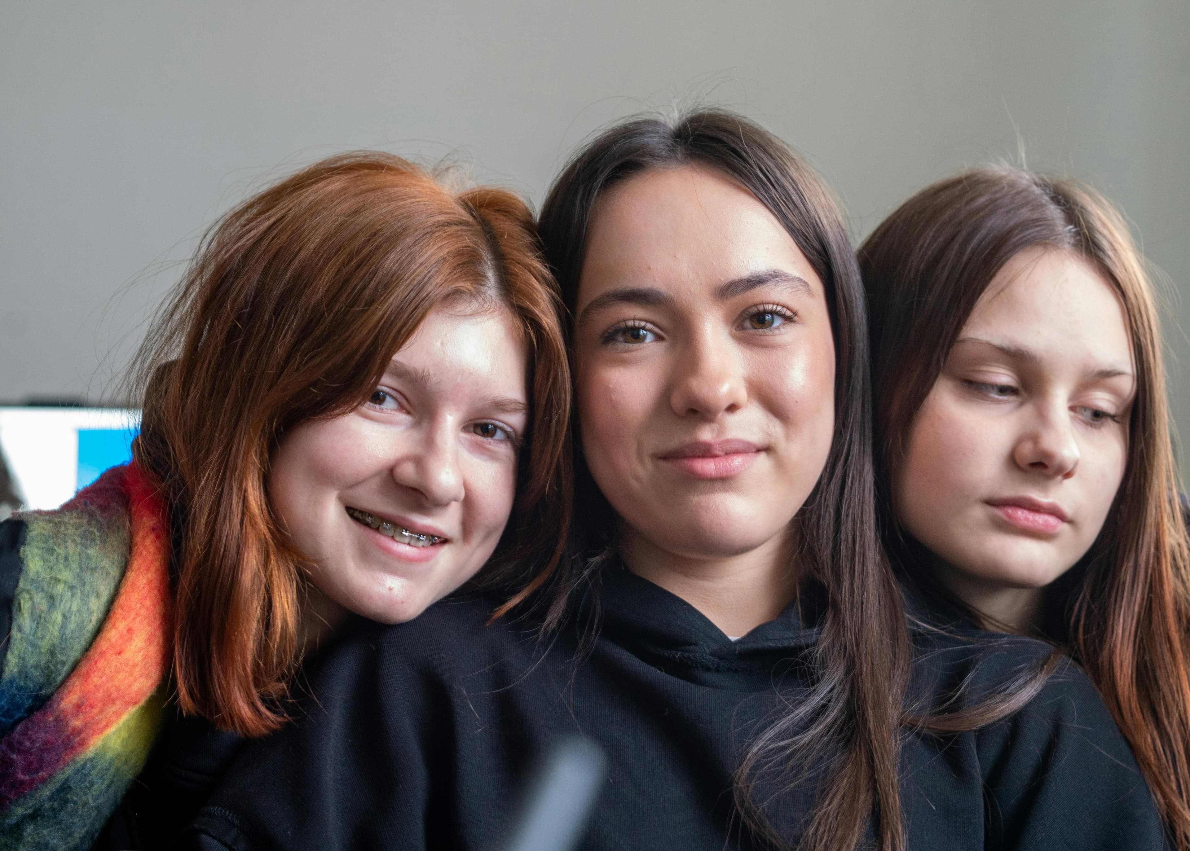 Three young women with red, dark, and brown hair pose together for a group portrait.