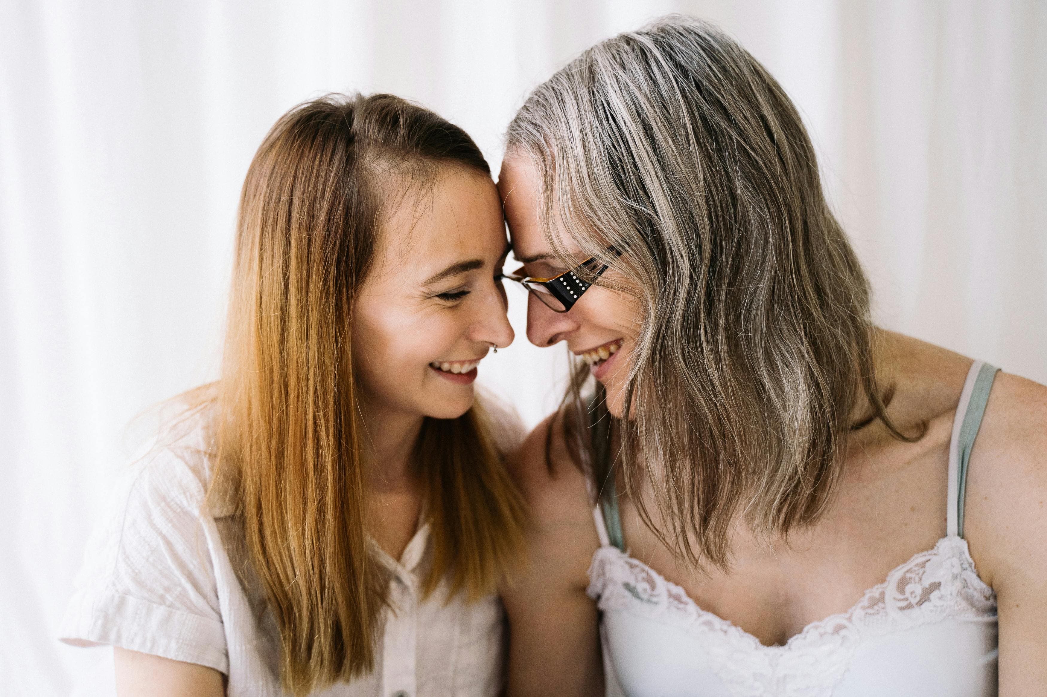 A young woman and an older woman lean their foreheads together, sharing a joyful laugh.
