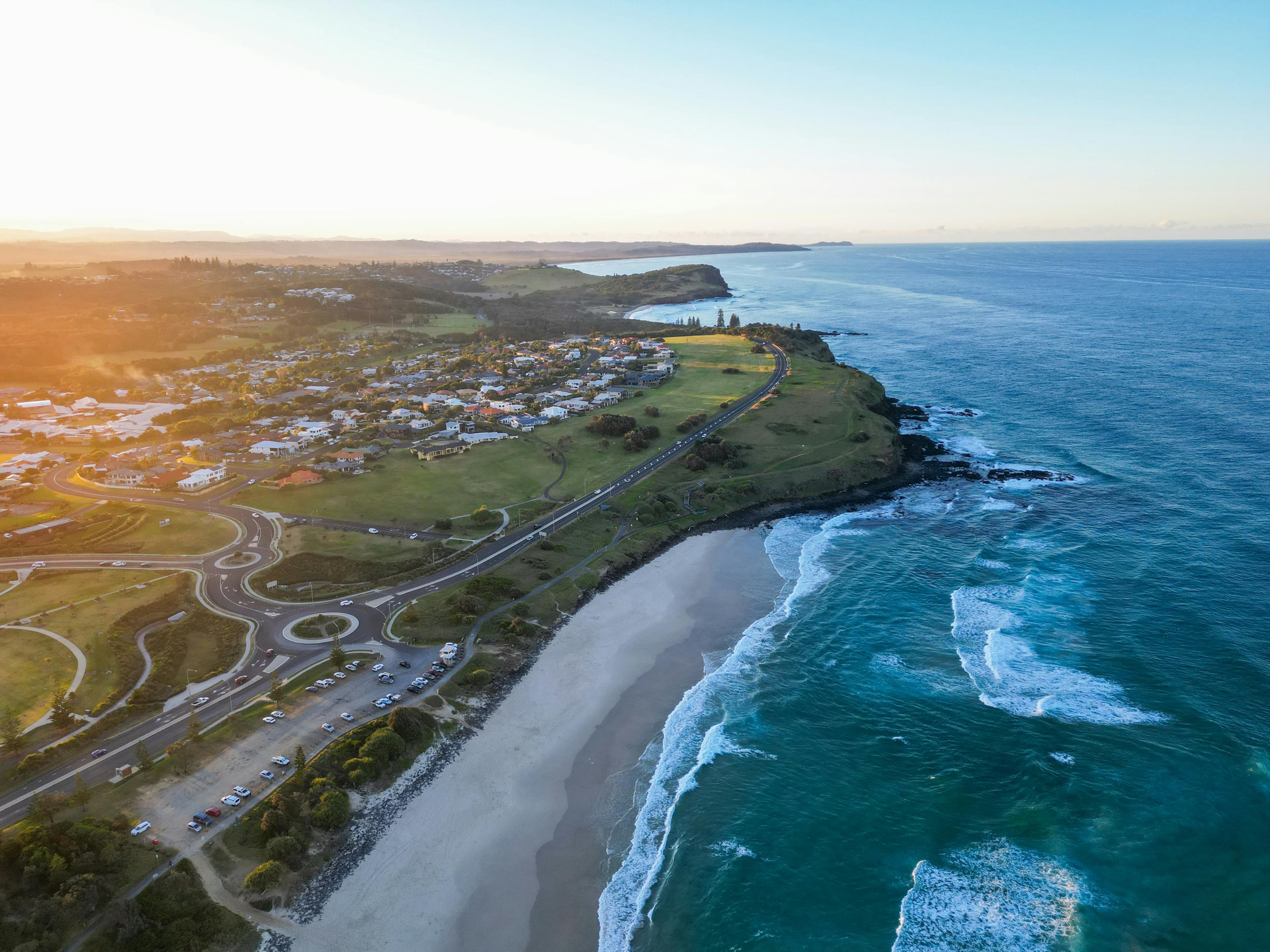 Sunset aerial view of a coastal town, sandy beach, and turquoise ocean waves.