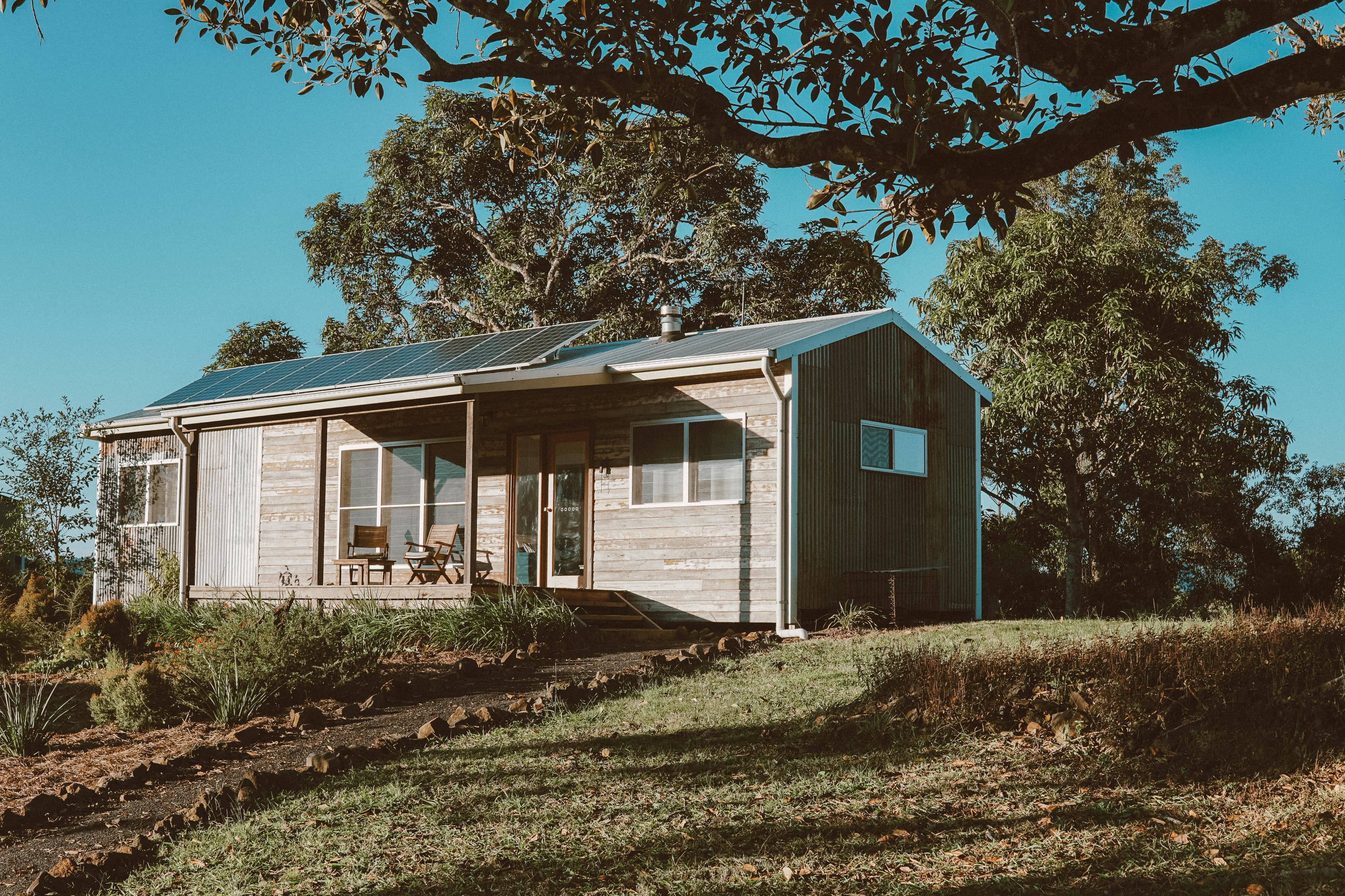 Rustic wooden cabin with solar panels, surrounded by trees and a grassy lawn.