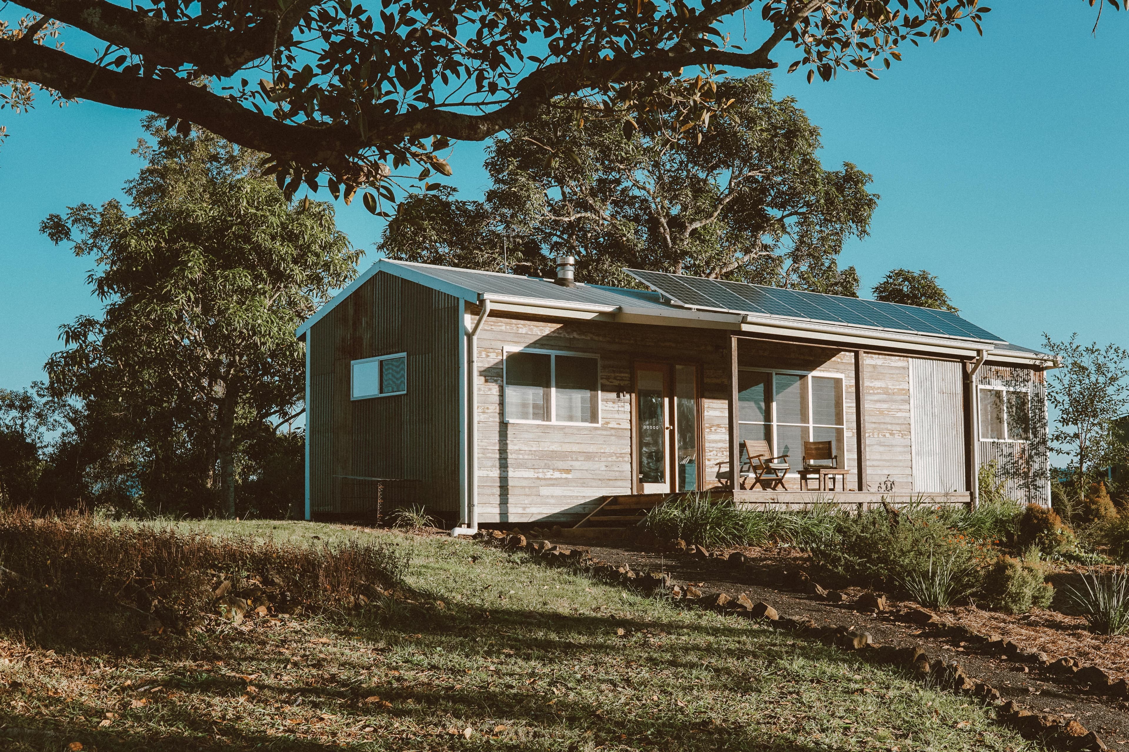 Rustic wooden cabin with solar panels, nestled among trees in a sunny, rural landscape.