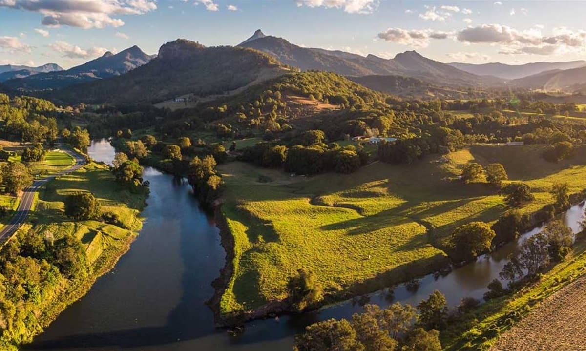 Aerial view of a winding river through a lush green valley with mountains at sunset.