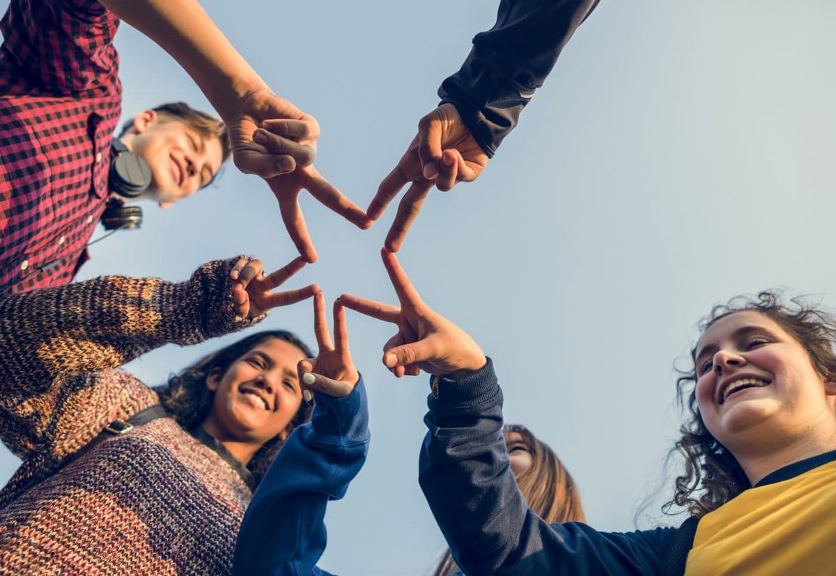 Diverse group of smiling friends forming a star with their fingers against a blue sky.